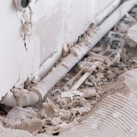 Shabby wall and drainage water pipe near hole in broken floor in bathroom